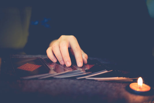 A hand rests on spread out tarot cards, all face down. A candle is burning in the corner. 